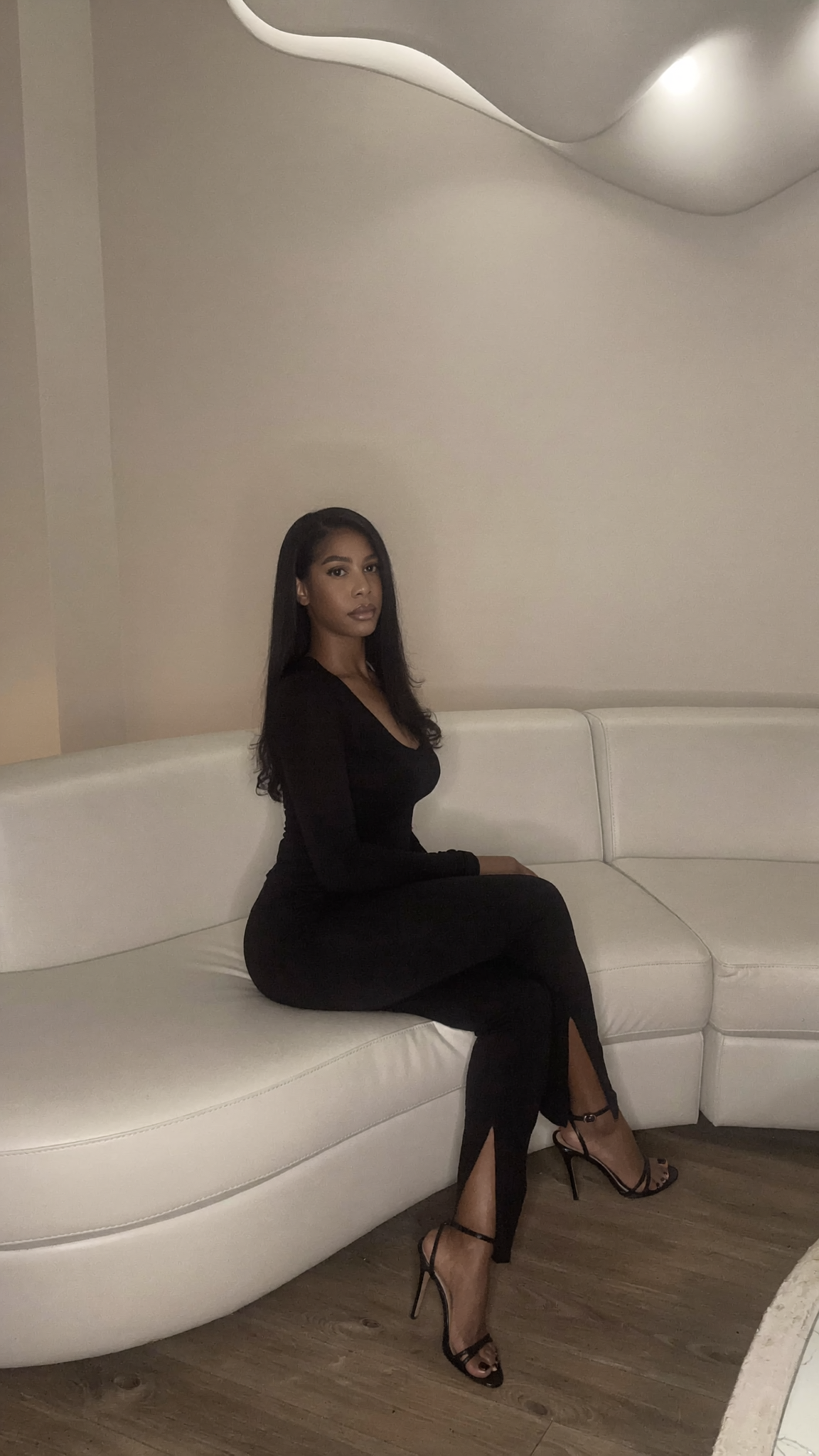 Coco in a black dress seated on a cream sofa